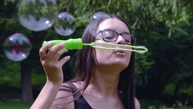 Teenage girl blowing soap bubbles and having fun in summer time. 4k hand held movement