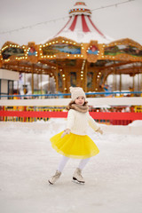 Child young girl ice skating at the ice rink outdoor. The girl in the yellow skirt