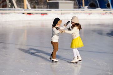 Young girl and boy ice skating at the ice rink outdoor. The girl in the yellow skirt