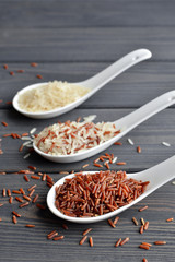 Mixed organic raw rice in ceramic spoons over dark desk background