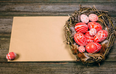 Easter eggs with white pattern inside bird nest on right side of old sheet of paper on wood board. Top view horizontal background. - obrazy, fototapety, plakaty