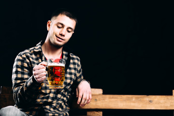 a man with a glass of beer sitting on a bench on a black background