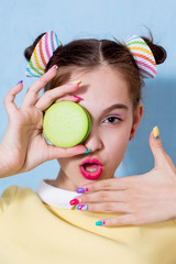 A portrait of a young girl, one eye covered by a green macaroon cake. A woman is surprised and opens her mouth.