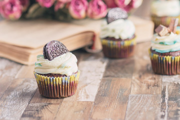 Handmade chocolate muffins with decorations. Book and a bouquet of roses, blurred background