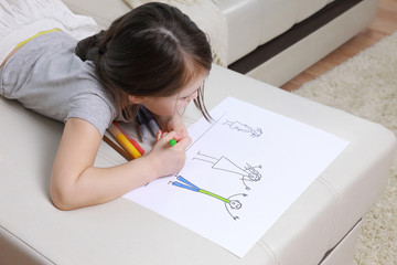 Girl in bright clothing draws a picture of the family. Light room