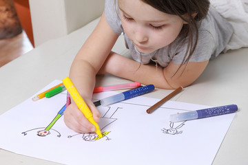 Girl in bright clothing draws a picture of the family. Light room