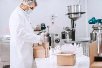 Portrait of chemical worker in sterile uniform packing liquid soaps in boxes. Chemical factory interior.