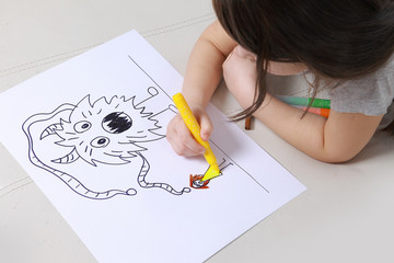 Girl in bright clothing draws a picture of the family. Light room. childhood fears