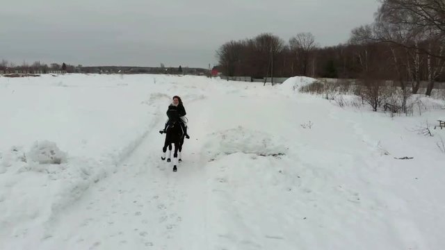 A young smiling woman riding a horse on a snowy field