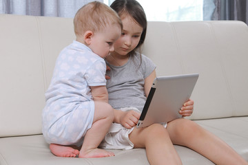 Children sit and play a game on the tablet and phone, boy and girl enthusiastically looking at the screen