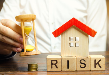 Businessman holds clock, wooden house and the inscription Risk on wooden block. The concept of non-payment of interest rates on mortgages. Real estate investment risk. Loss of property for non-payment