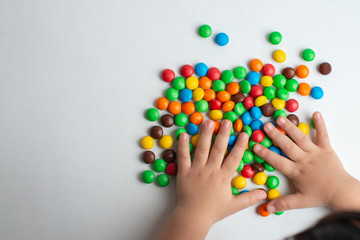 Colorful chocolate candies on white background with child hand