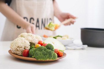 Woman in kitchen cooking stir vegetables on pan and tasting.