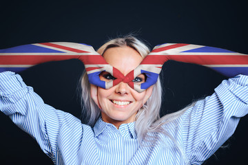 A girl with a painted UK flag on her hands makes a mask with her hands and looks through her fingers, making faces, fooling around. Making the gesture of a mask or the like binoculars , eyes looking t