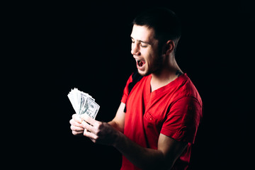 a man in a red t-shirt on a black background with a pack of money emotionally reacts