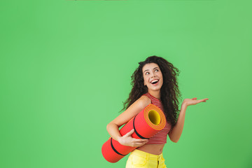 Photo of athletic woman 20s smiling and carrying yoga mat during workout