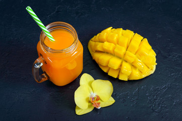 Mango smoothie in a glass jar and fresh mango on a black background. Mango shake. Tropical fruit...