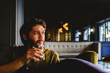 Young man with latin beard looking to infinity thinking about future business with a drink in his hand.