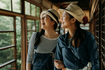 two asian female travelers in straw hats smiling laughing sightseeing spring garden view while...