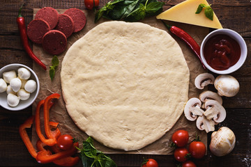 pizza base, dough with ingredients on wooden background