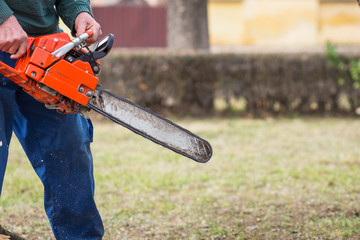 Old man in blue pants hold orange chainsaw with his bare hands.
