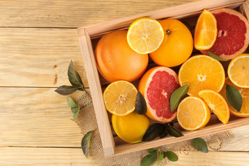 Obraz na płótnie Canvas Citrus fruit. various citrus fruits with leaves of lemon, orange, grapefruit in a box on a natural wooden table. top view