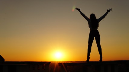 Fototapeta premium Young girl in sports uniform sits on the edge of the roof during sunset.
