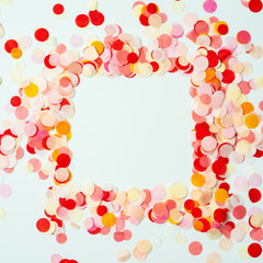 Colorful frame made with red and orange festive confetti on pastel background