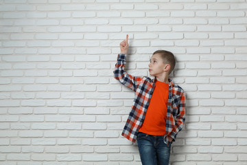 Cute stylish boy near white brick wall . boy points Finger at something isolated on white background. Portrait of a caucasian boy in jeans and a shirt in a cell. boy shows something with a finger.