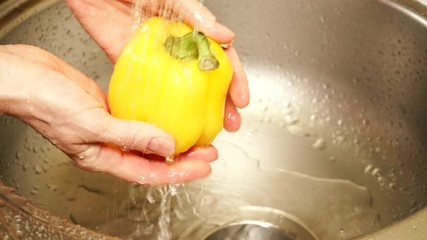 Female hand washing fresh yellow paprika vegetable in kitchen sink under water stream. Cleaning products. Ingredient for cooking or tasty salad. Healthy eating, dieting concept - Powered by Adobe