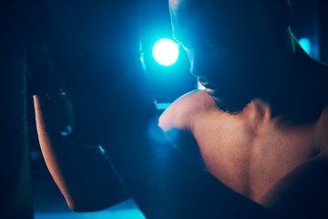 Close-up portrait of concentrated boxer on the ring. Studio shot, blue light. Light projectors behind man
