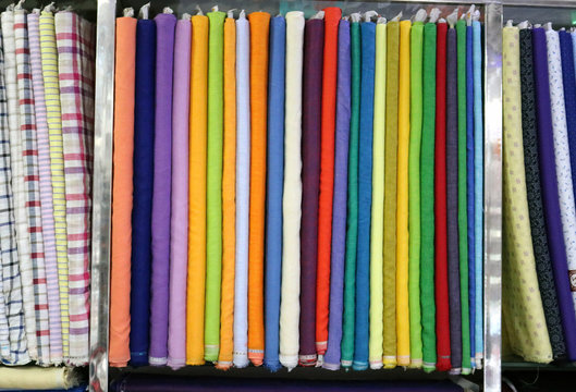 A textile multicolored wrapped raw cloth bundles in rack stand used to make finished products like shirts and paints etc.