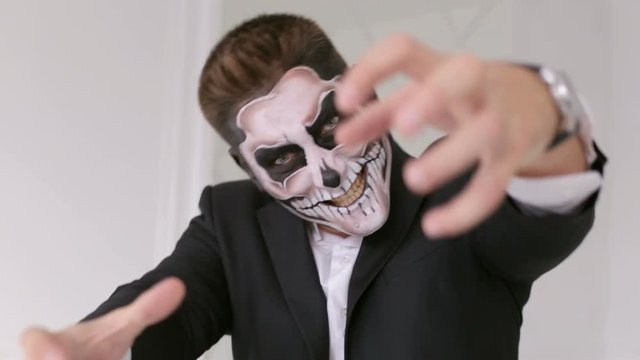 Businessman with make-up skeleton creepy looking at the camera, and stretches his hands to the camera. Halloween or horror theme. Dead face make up portrait of young man in studio.