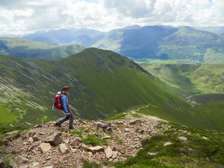 Fototapeta na wymiar A female hiker and their dog descending from Grasmoor down Lad Hows above Buttermere on a sunny day in the English Lake District, UK.
