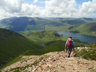 Fototapeta na wymiar A female hiker and their dog descending from Grasmoor down Lad Hows above Buttermere on a sunny day in the English Lake District, UK.