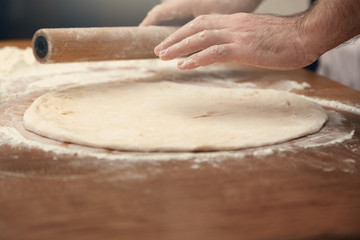  A man is cooking pizza. Closeup of male hands and dough.