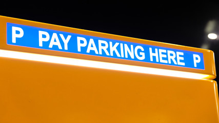 white pay parking sign against blue background on yellow payment machine at night urban transportation toll point terminal to collect money for park place