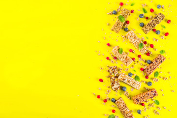 Cereal granola bars with nuts, fruits and berries, bright yellow background top view copy space