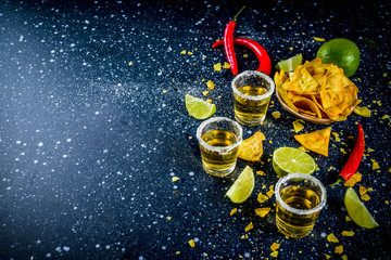 Cinco de Mayo celebration concept. 5th May Mexican party's drinks - margarita cocktail, tequila shots with lime, hot chili peppers and chips, dark background copy space - obrazy, fototapety, plakaty