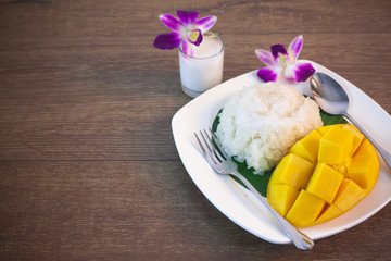 Thai dessert, mango and sticky rice with coconut milk on a wooden background