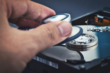 hand holding stethoscope for diagnose old dusty disassembled hard drive from the computer over dark background