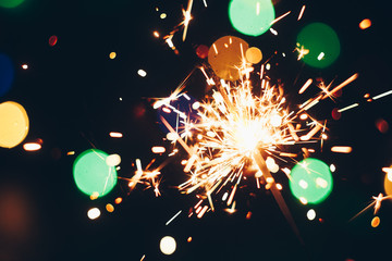 sparkling Bengal sparklers sticks in flames on a black background with lights bokeh. christmas...