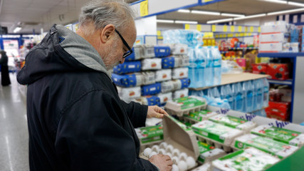 Sale, shopping, consumerism, people concept. Old man shopping and choosing food products in supermarket. Financial management with economic foods. Trying to find the best in terms of price and quality