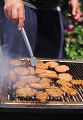 Men's hands cooking delicious grilled meat (burgers, sausages) during barbecue party on a summer day 