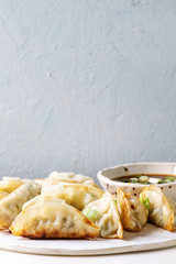 Fried asian dumplings Gyozas potstickers in white ceramic plate served with bowl of soy onion sauce over white marble table. Grey wall at background. Asian dinner