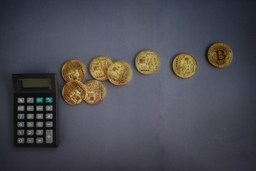 Top view of calculator and golden replica of bitcoin on dark vignette grey background.