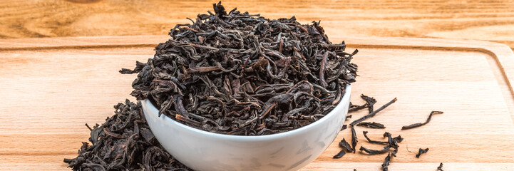 Dried tea is poured into a ceramic cup on a wooden plank table.