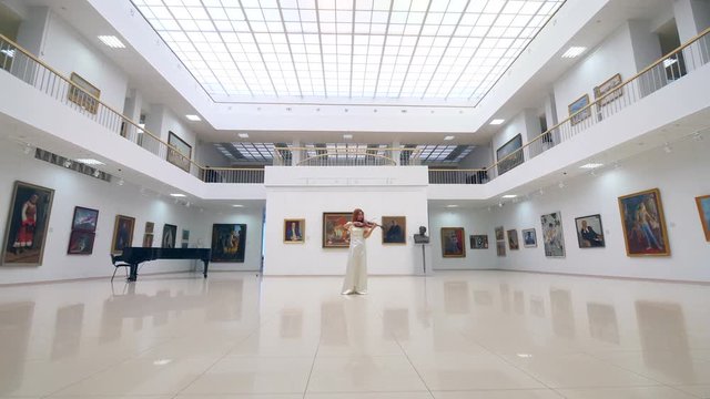Woman plays wooden violin in a big room in museum.