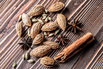 Cinnamon sticks, cardamom, almonds and star anise on a brown wooden surface.