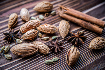Cinnamon sticks, cardamom, inshell almonds and star anise on a brown wooden surface.